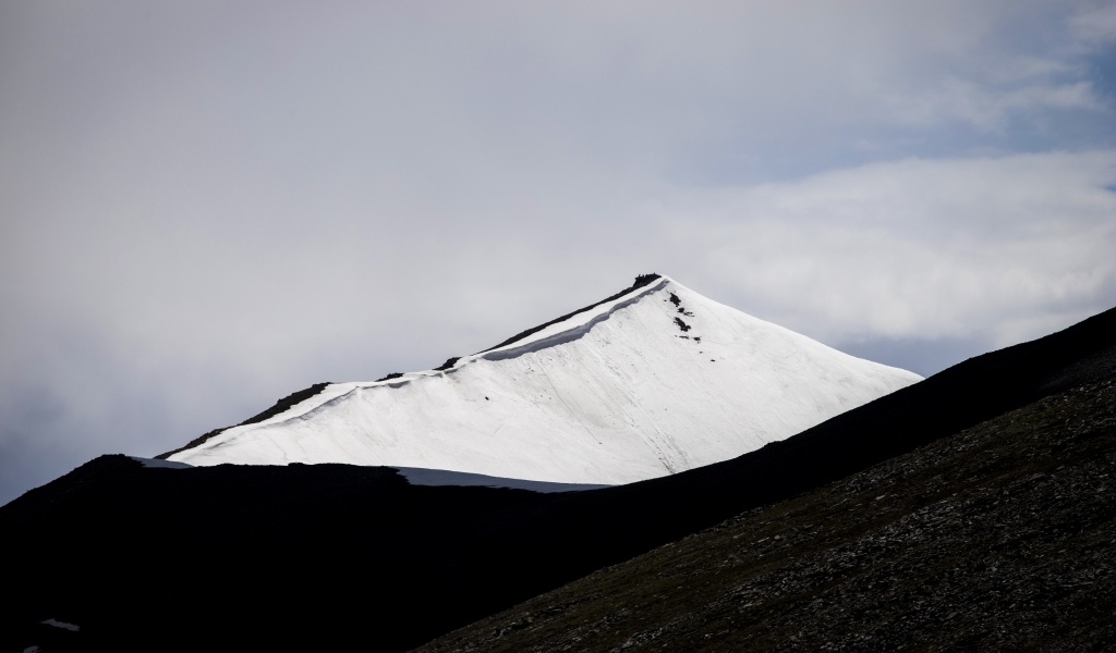 Заснеженная вершина горы под грозовым небом