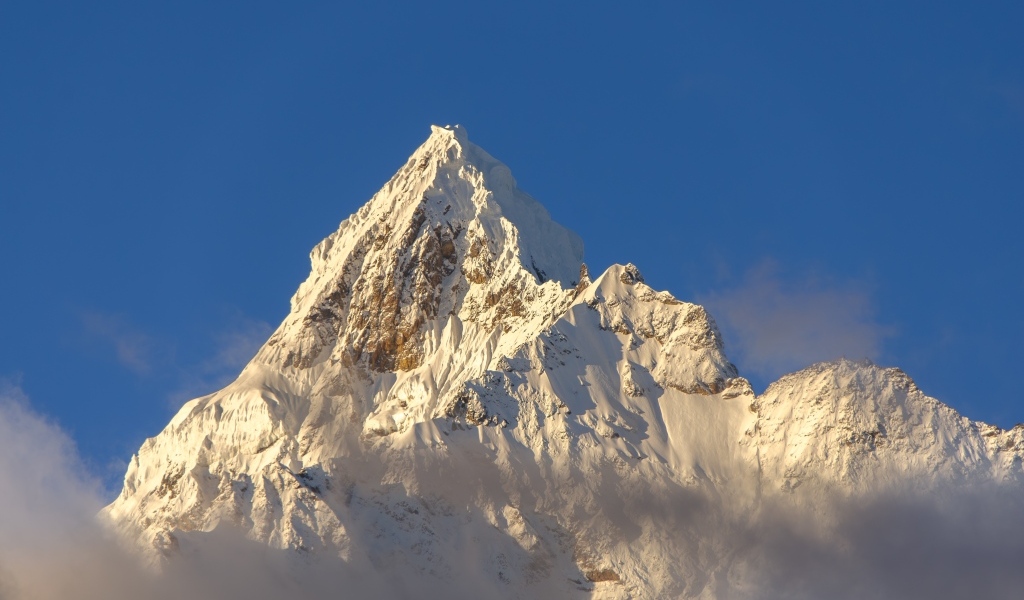 Крутая заснеженная вершина горы на голубом фоне