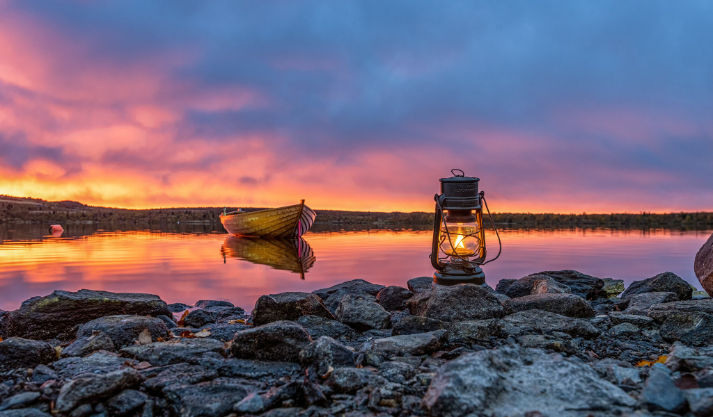 Керосиновая лампа стоит на камнях у озера