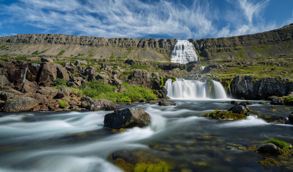Водопад стекает с гор на фоне красивого голубого неба Исландии