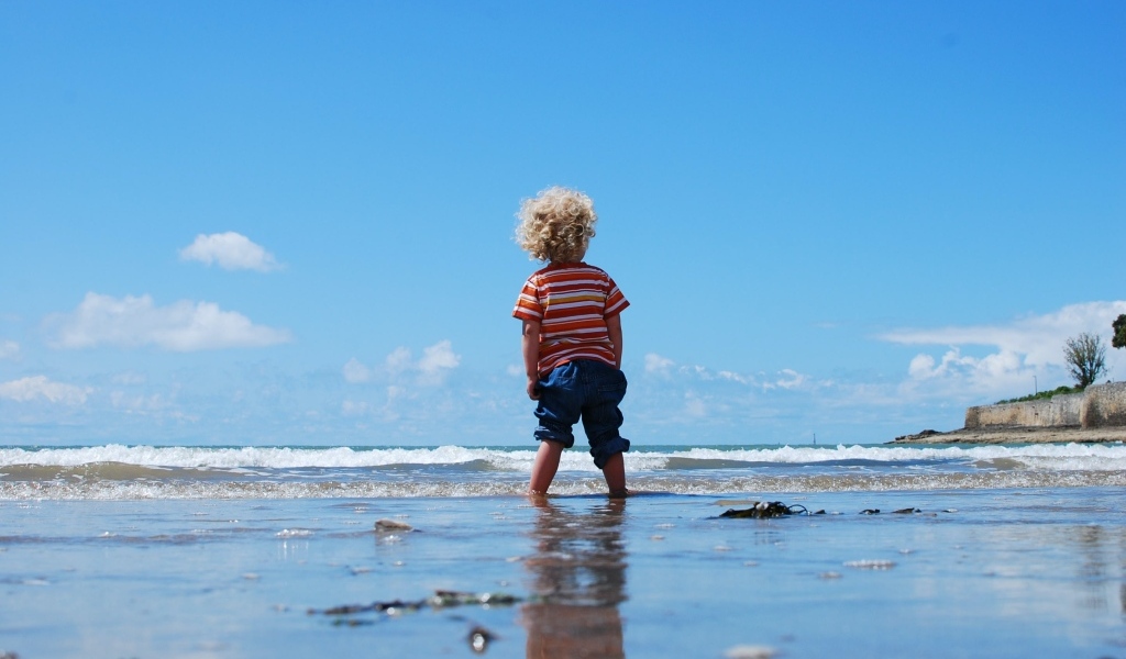 Маленький мальчик гуляет по мокрому песку у моря