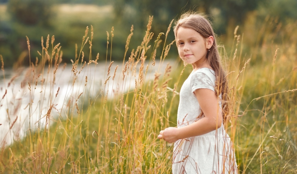 Маленькая девочка в белом платье гуляет по высокой траве