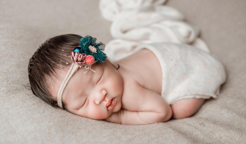 Новорожденная девочка азиатка спит на сером покрывале