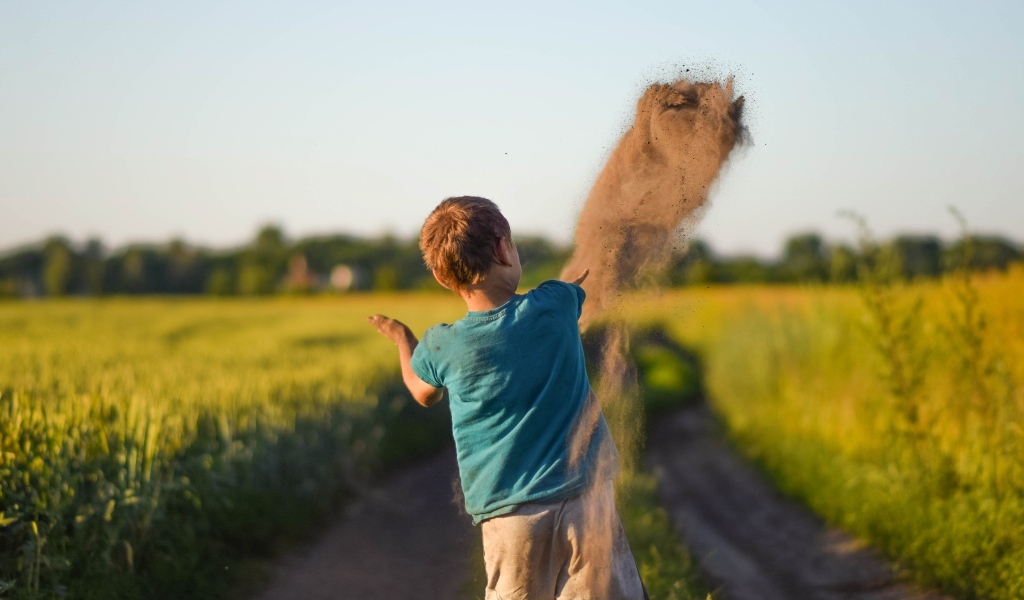 Мальчик бросает песок на дороге