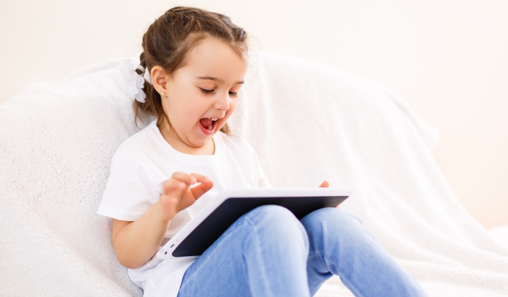 Веселая девочка с планшетом на кровати 