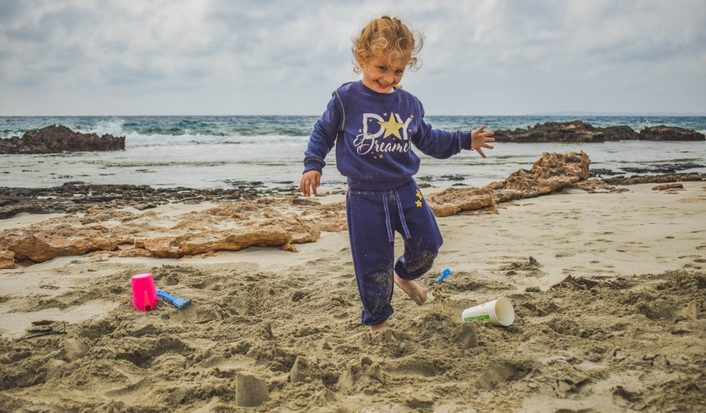 Веселая девочка играет на песке на пляже