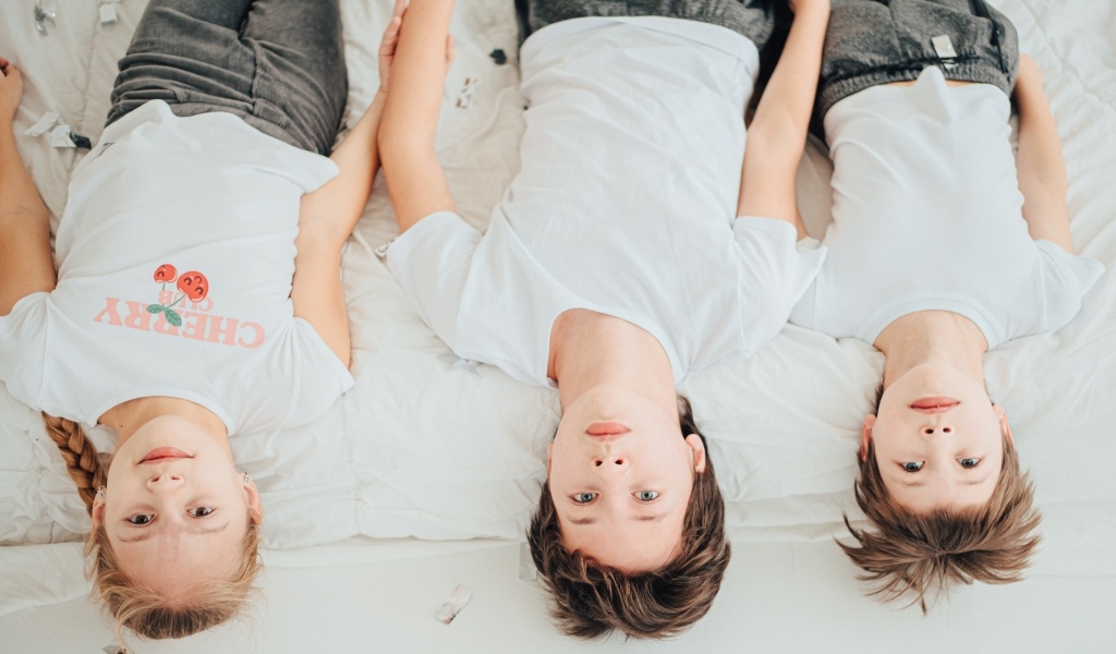 Дети в белых футболках лежат на кровати