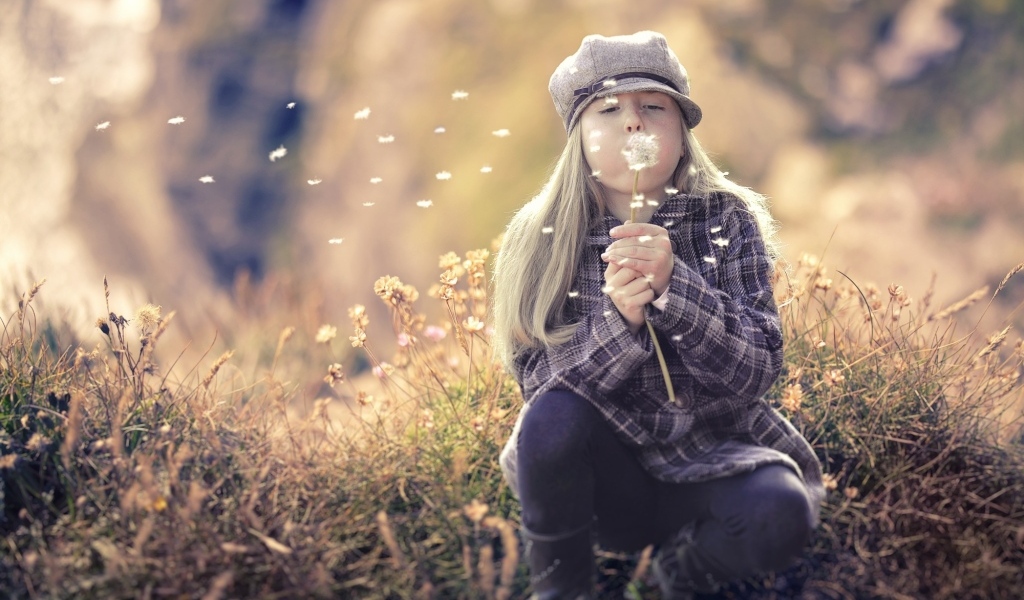 Девочка в кепке сдувает одуванчик