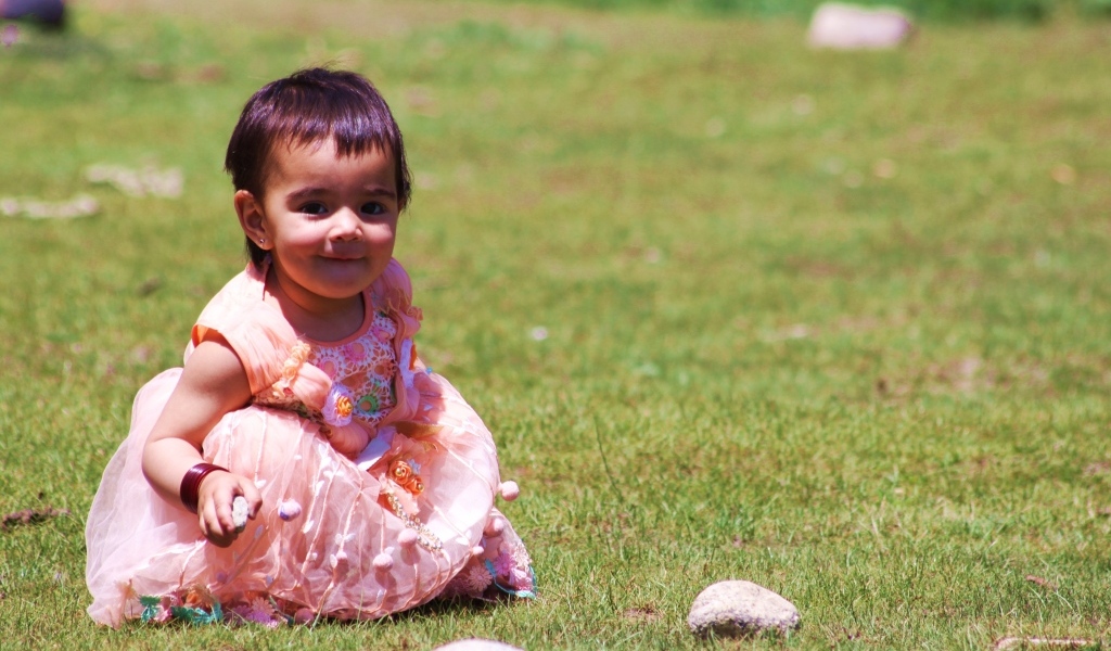 Девочка в розовом платье играет на зеленой траве