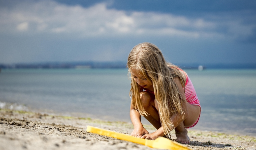Девочка играет на песке у моря