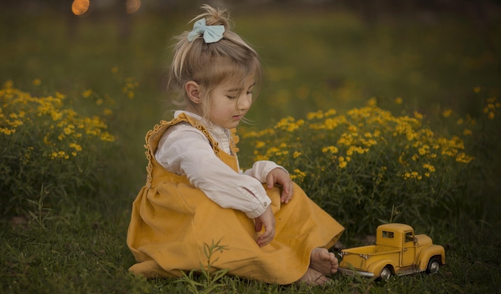 Девочка сидит на траве с игрушечной машинкой