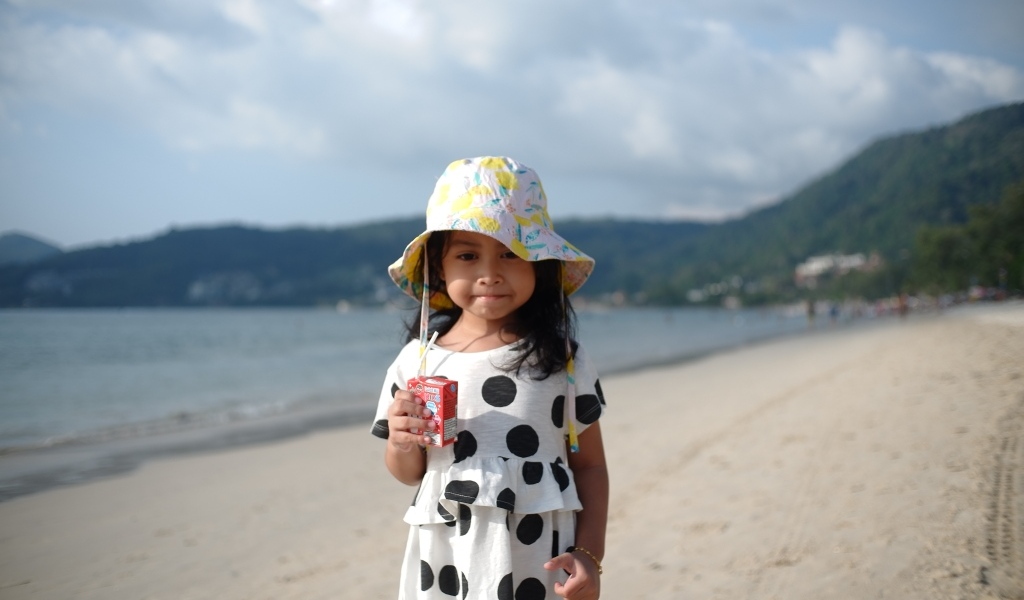 Девочка с соком в руках стоит на пляже