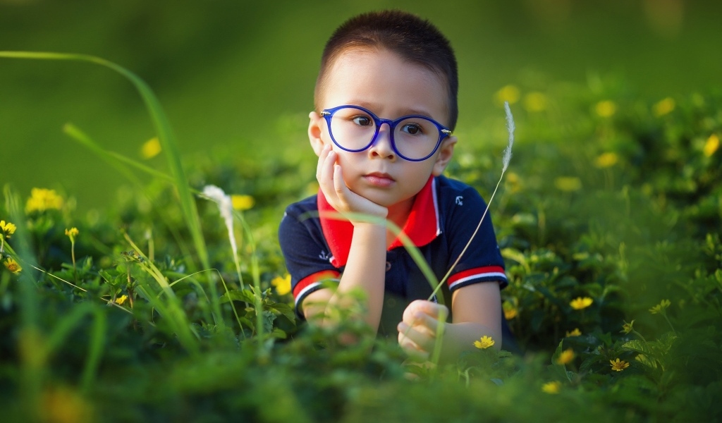 Маленький мальчик в очках лежит на траве