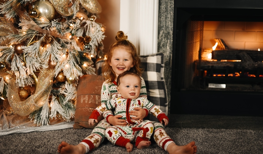 Маленькие брат и сестра сидят у новогодней ели