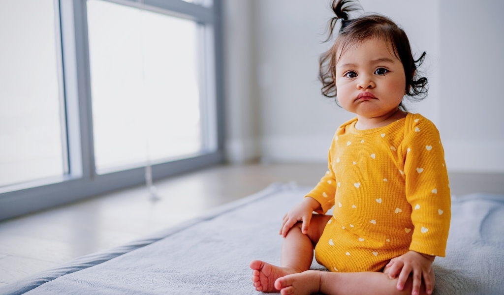 Маленькая смешная девочка сидит у окна