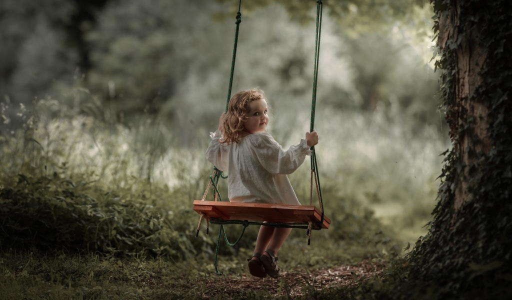 Маленькая девочка на качели в саду
