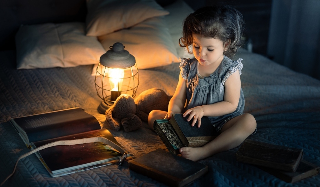 Маленькая девочка читает книги на кровати