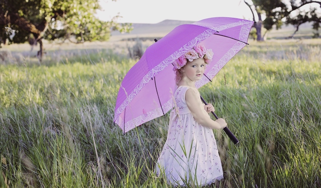 Маленькая девочка стоит в траве с зонтом