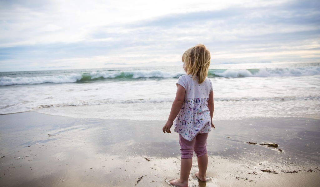 Маленькая девочка стоит на берегу моря