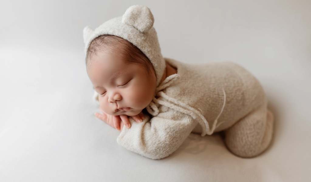 Маленький спящий ребенок в вязаном костюме на сером фоне