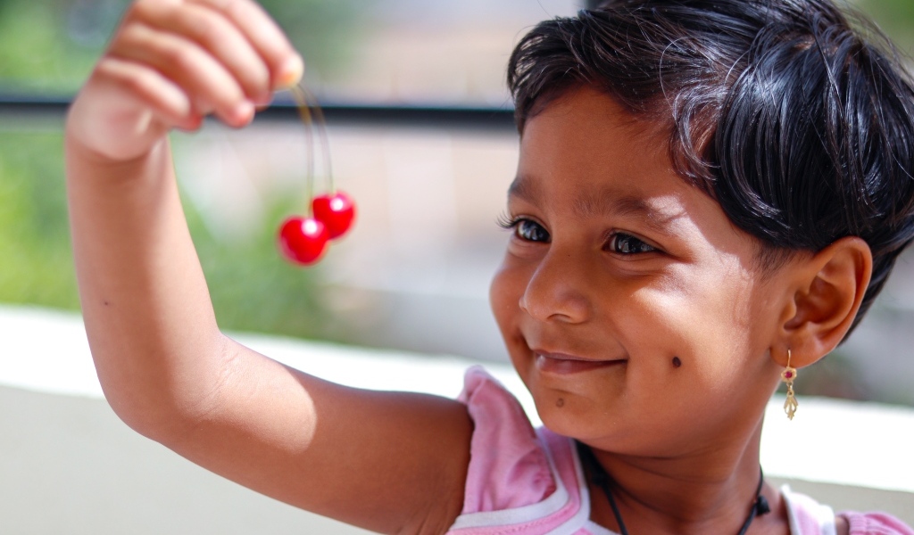 Маленькая улыбающаяся девочка с ягодами вишни в руках