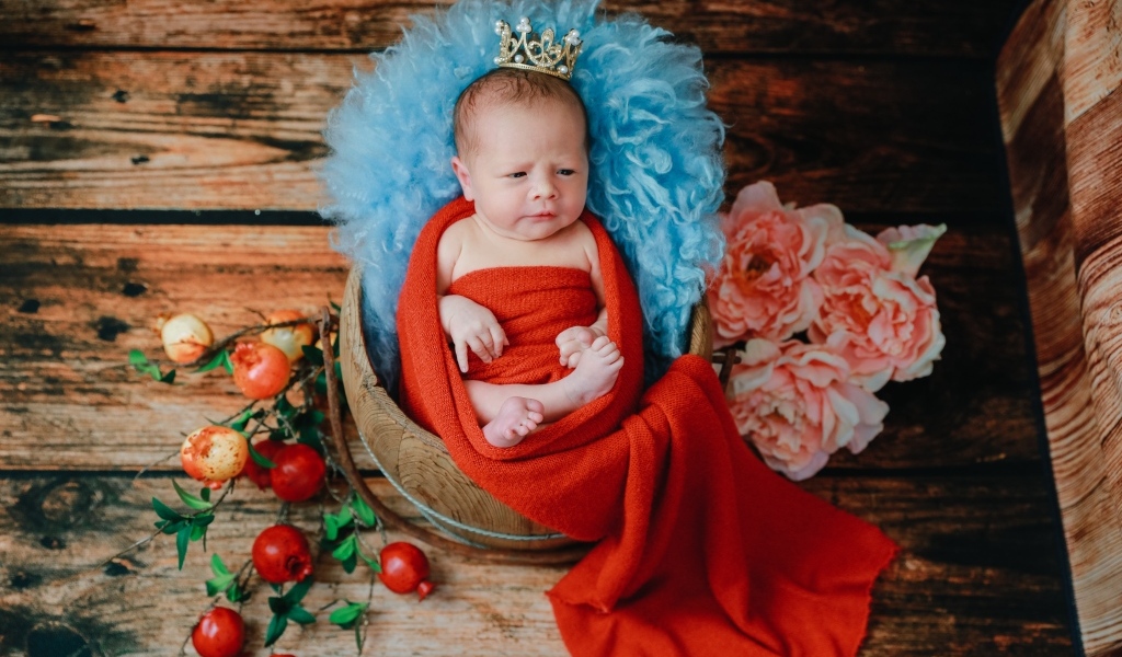 Новорожденный ребенок в красном покрывале с короной на голове 