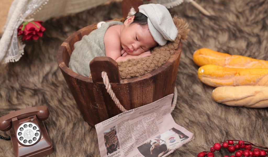 Новорожденный маленький мальчик в деревянном ведре на фотосессии 