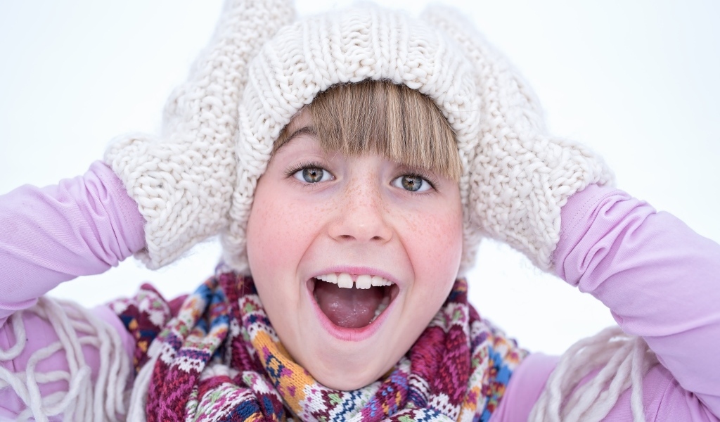 Довольная девочка в вязаной шапке и варежках
