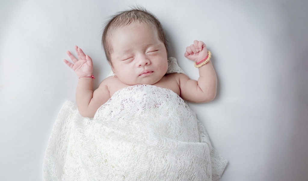 Маленький спящий ребенок на сером фоне под белым покрывалом