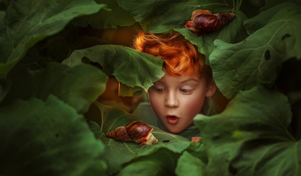 Удивленный рыжеволосый мальчик смотрит на улитку