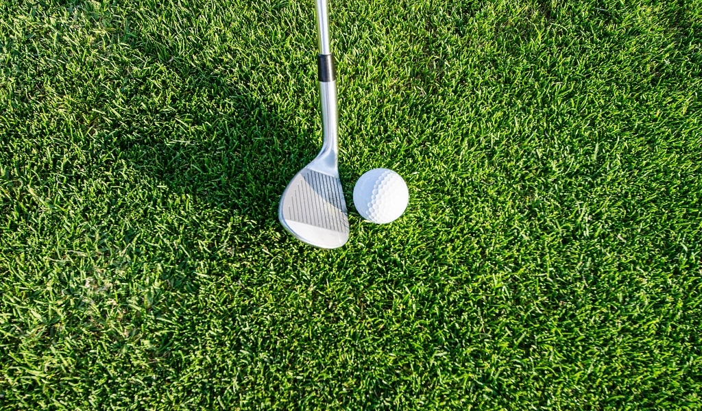 Клюшка и белый мяч для гольфа на зеленой  траве