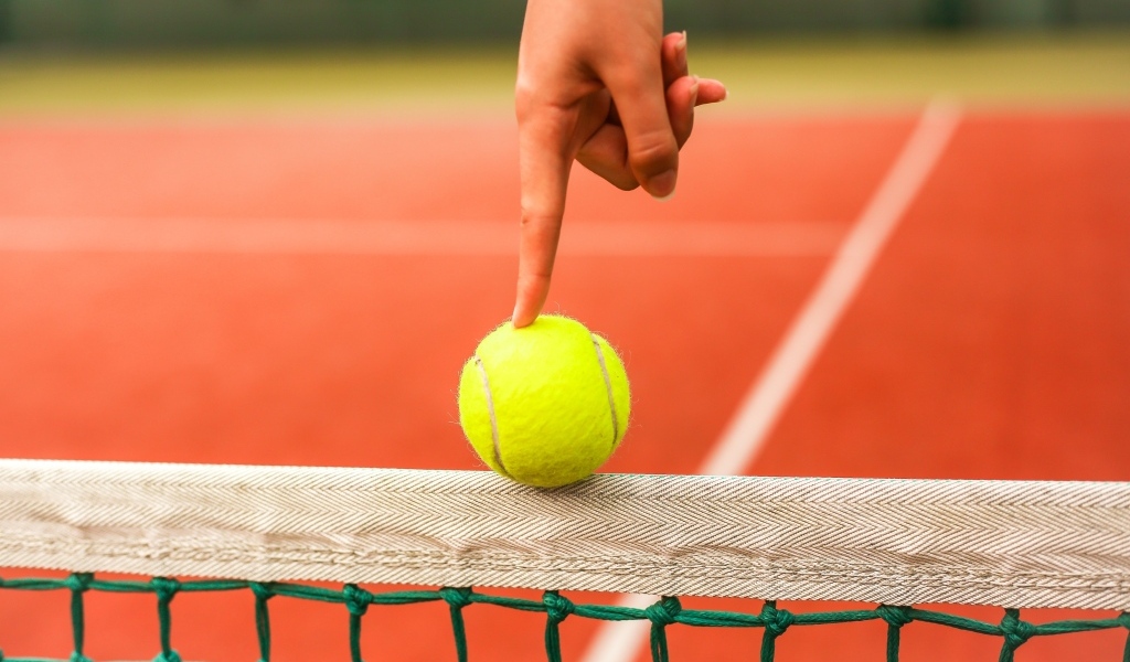 Палец держит желтый теннисный мяч