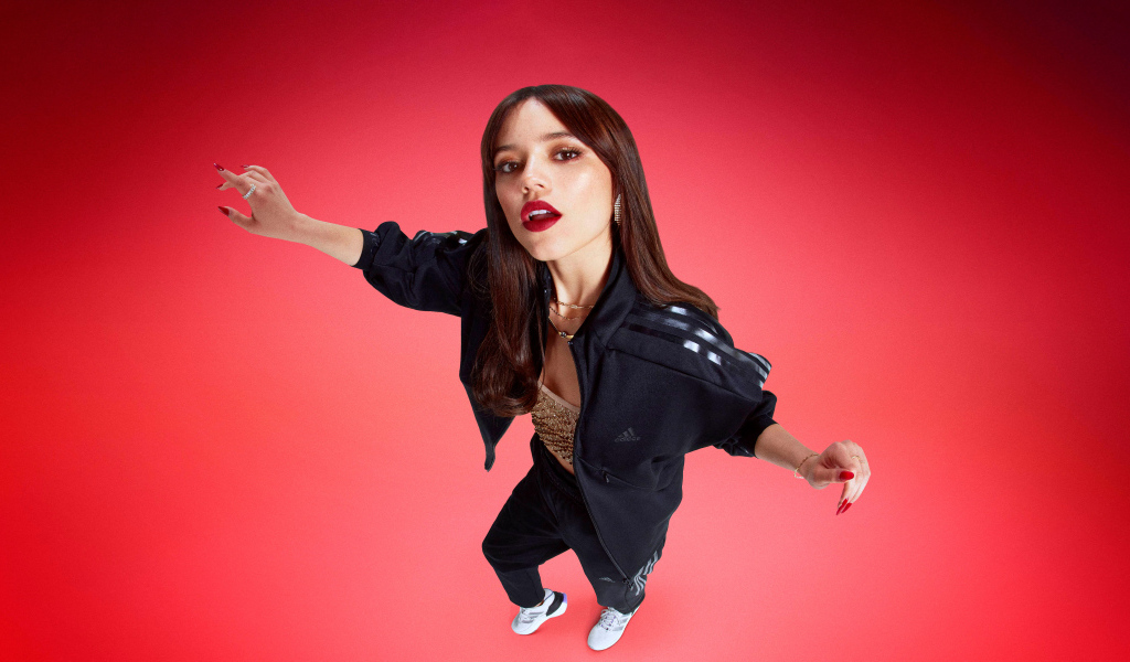 Молодая девушка актриса Дженна Ортега в спортивном костюме на красном фоне