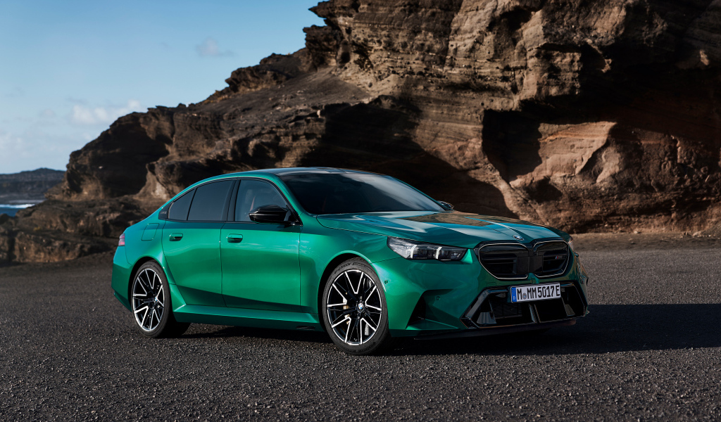 Зеленый автомобиль BMW M5 2024 года на фоне гор