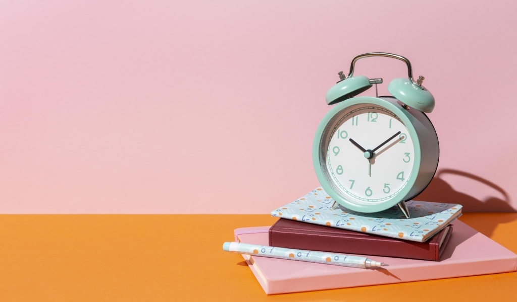 Будильник с книгами на розовом фоне