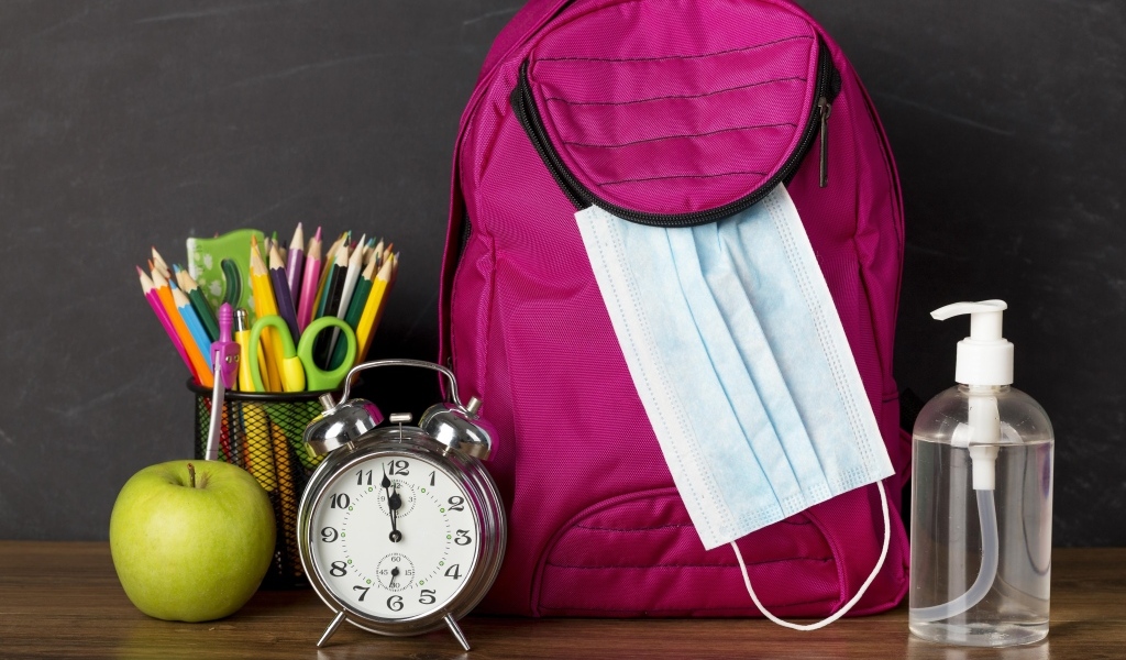 Рюкзак на столе с будильником, ручками и яблоком