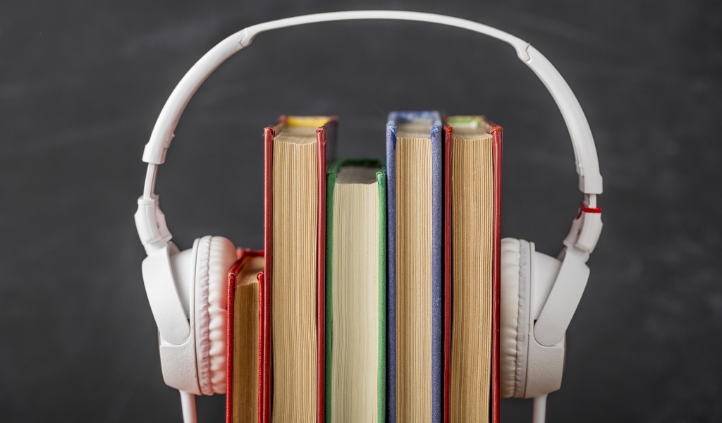 Разноцветные книги с белыми наушниками на сером фоне