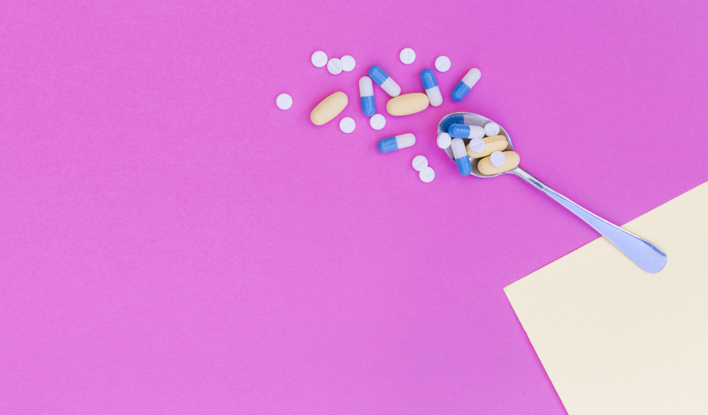 Таблетки с ложкой на розовом фоне
