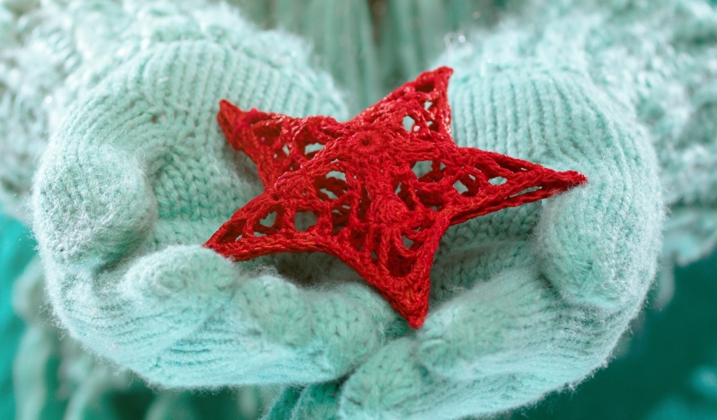 Красная вязаная звезда в руках в варежках