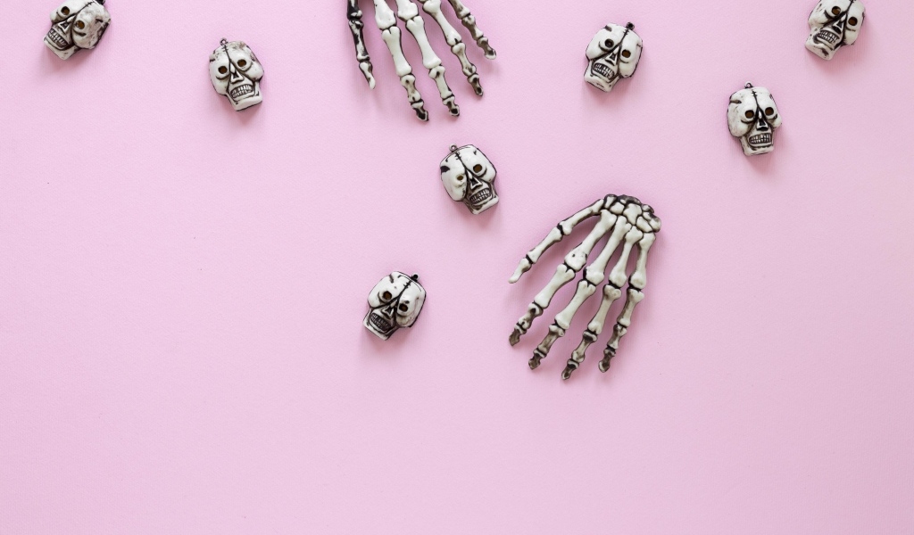 Кисти рук скелета и черепа на розовом фоне