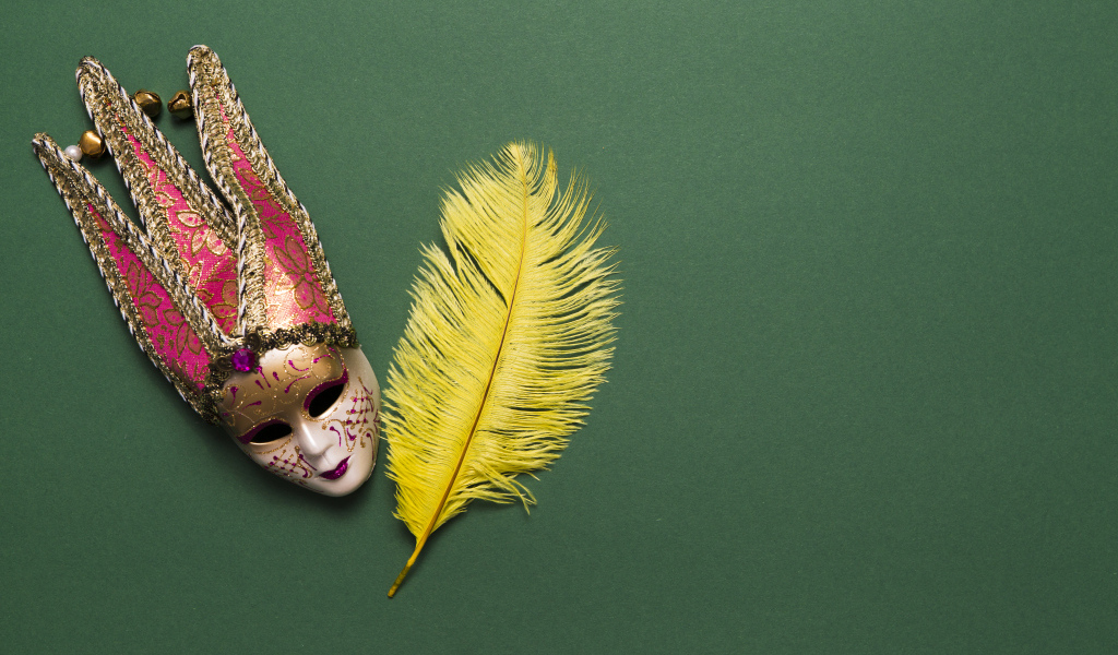 Венецианская маска и желтое перо на зеленом фоне