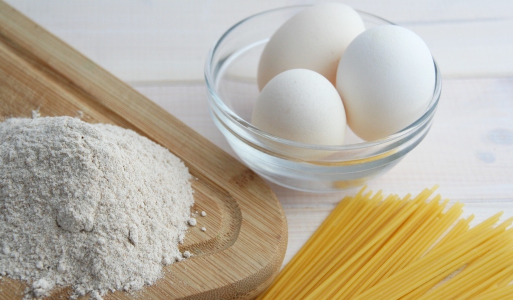 Яйца на столе с мукой и спагетти