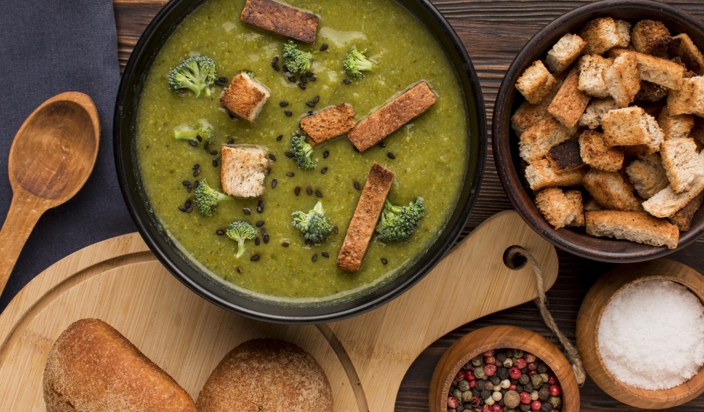 Зеленый суп пюре на столе с сухариками и перцем