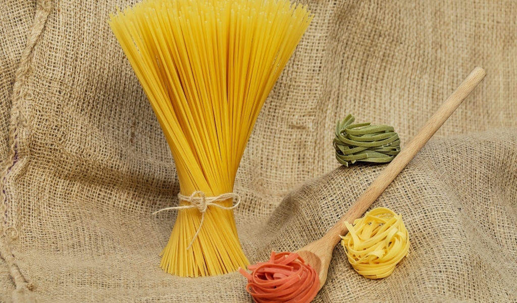 Разноцветные макаронные изделия с деревянной ложкой на мешке