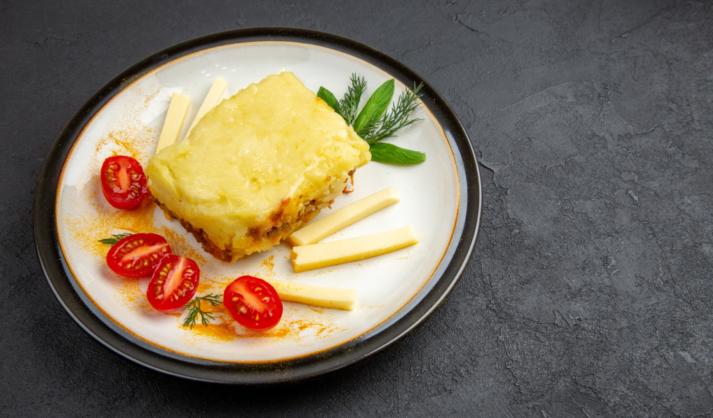 Кусок картофельной запеканки на тарелке с помидорами