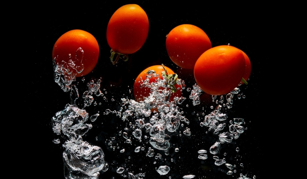 Красные помидоры в воде на черном фоне