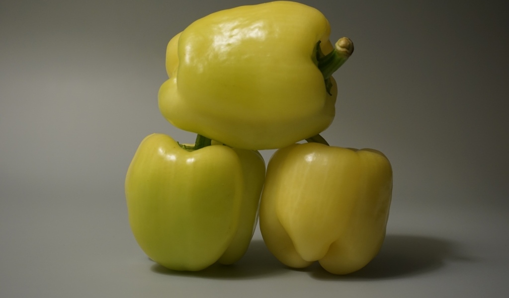 Три желтых перца на сером фоне