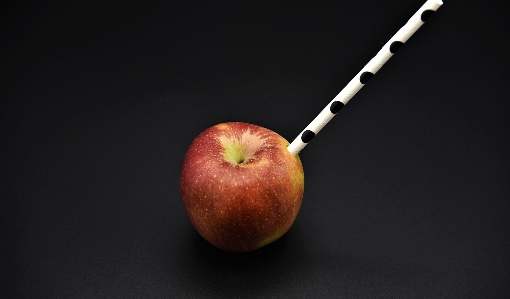 Большое красное яблоко с трубочкой на черном фоне