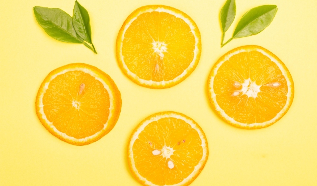 Нарезанный апельсин с зелеными листьями на желтом фоне