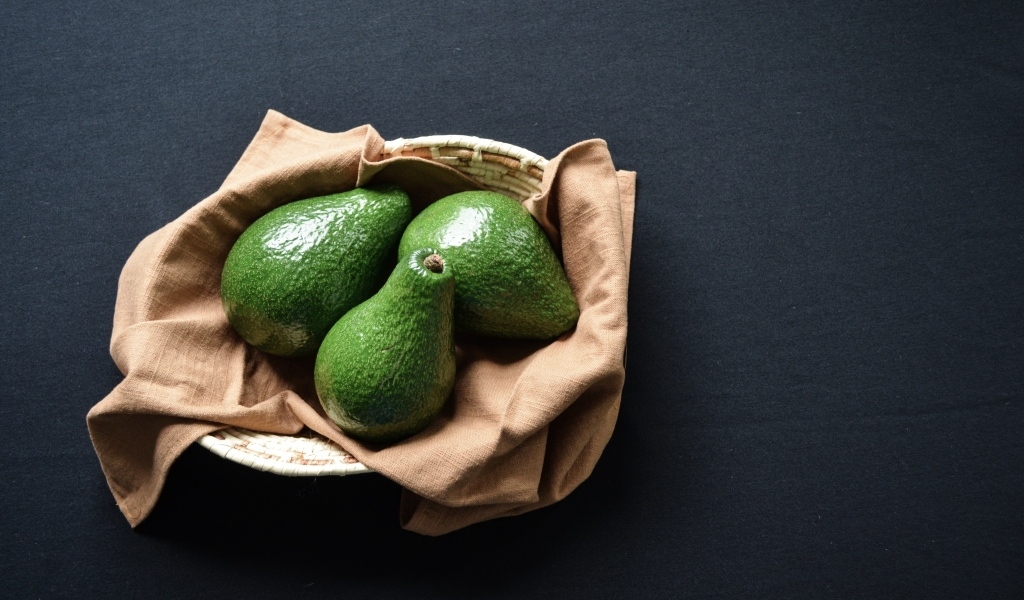 Три зеленых авокадо в корзинке на столе